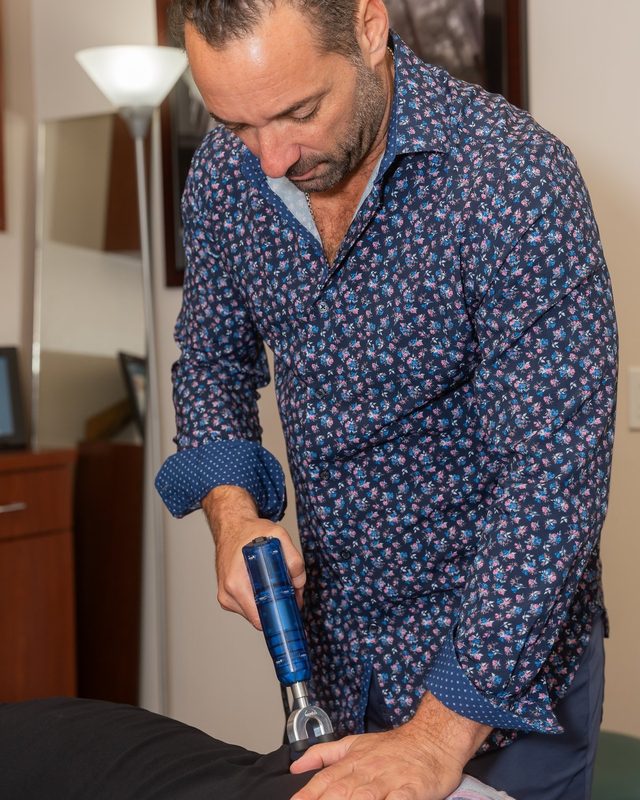 Dr. Esposito applying a handheld adjusting instrument to a patient's lower back.