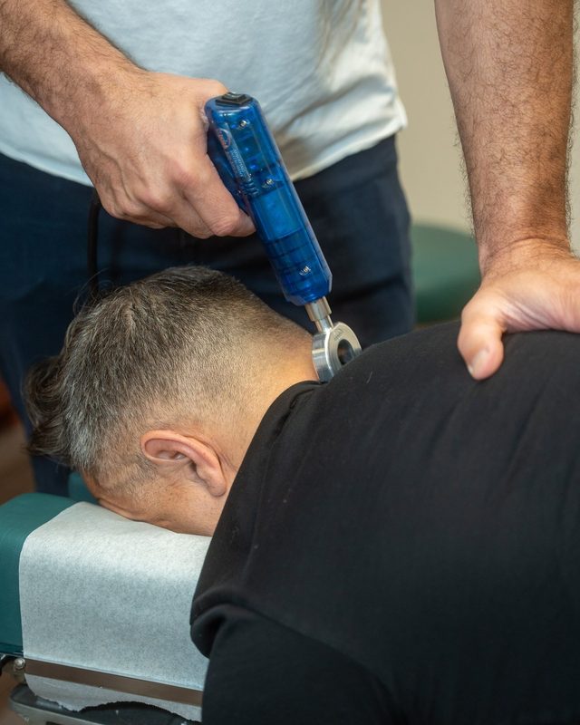 Dr. Esposito applying a handheld adjusting instrument at the base of a patient's neck.