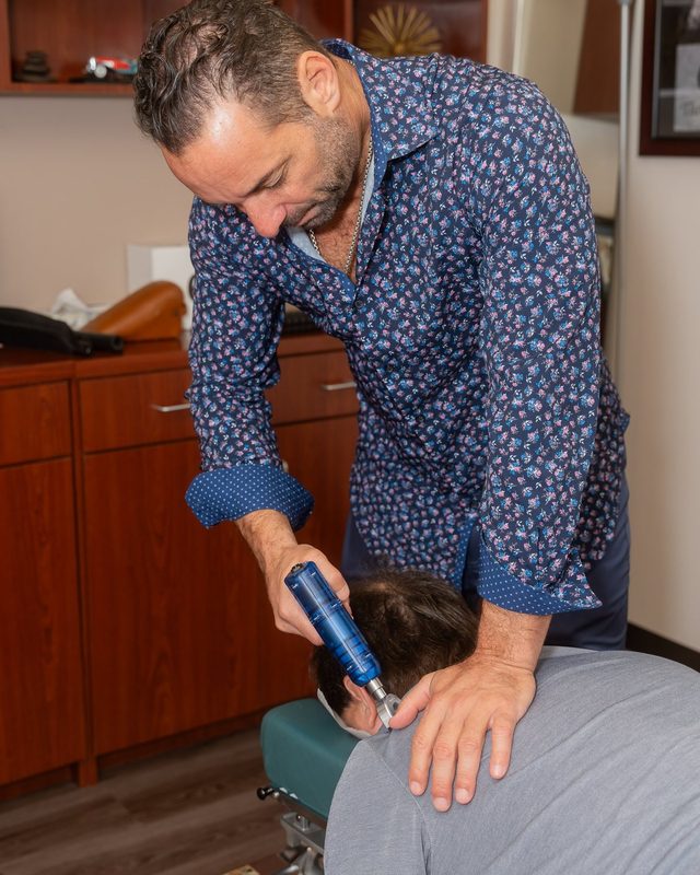 Dr. Esposito applying a handheld adjusting instrument to a patient's upper back.