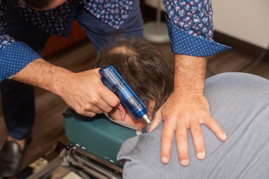 Dr. Esposito using a handheld adjusting instrument on a patient's upper back.