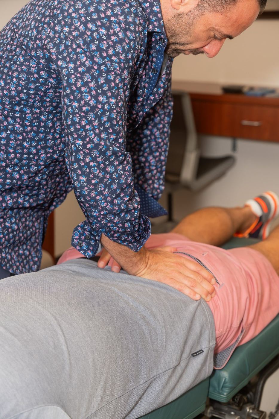 Dr. Edward Esposito pressing on a patient's lower back, spinal imaging displayed on a screen behind him.
