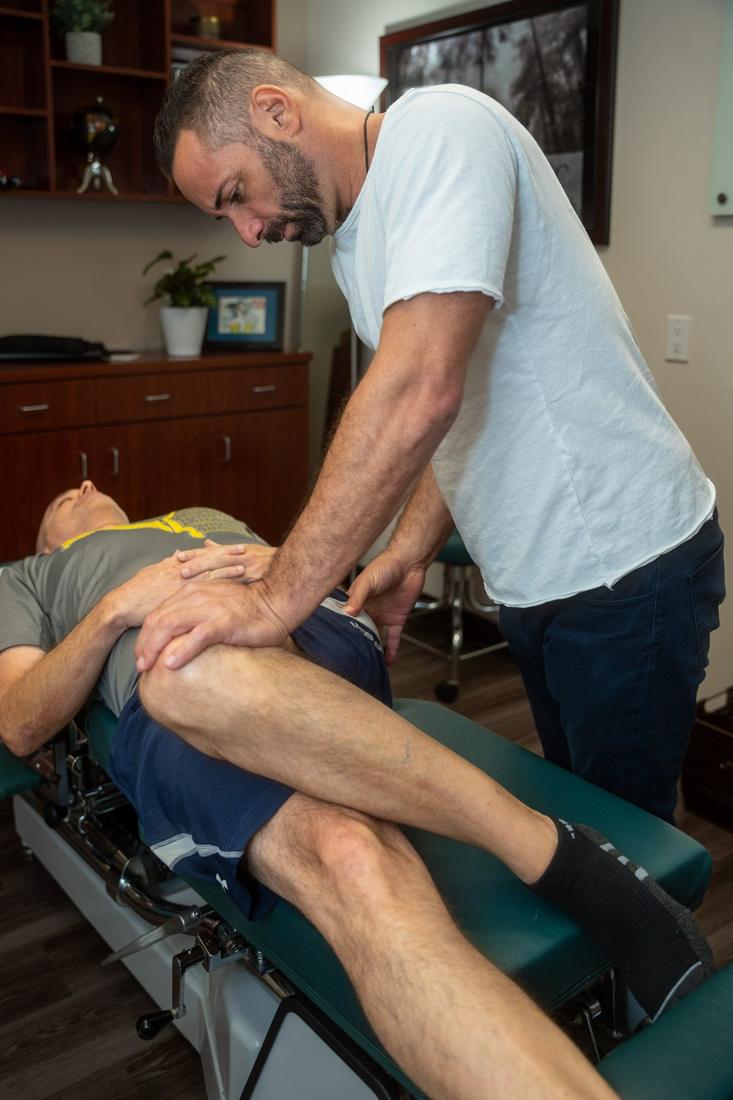 Dr. Edward Esposito guiding a patient's knee through a supine hip and leg stretch.