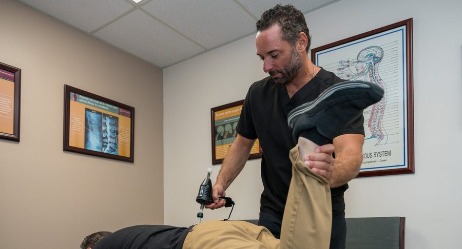 Dr. Esposito working on a patient's lower back and leg during an in-office visit, using a handheld adjusting instrument.