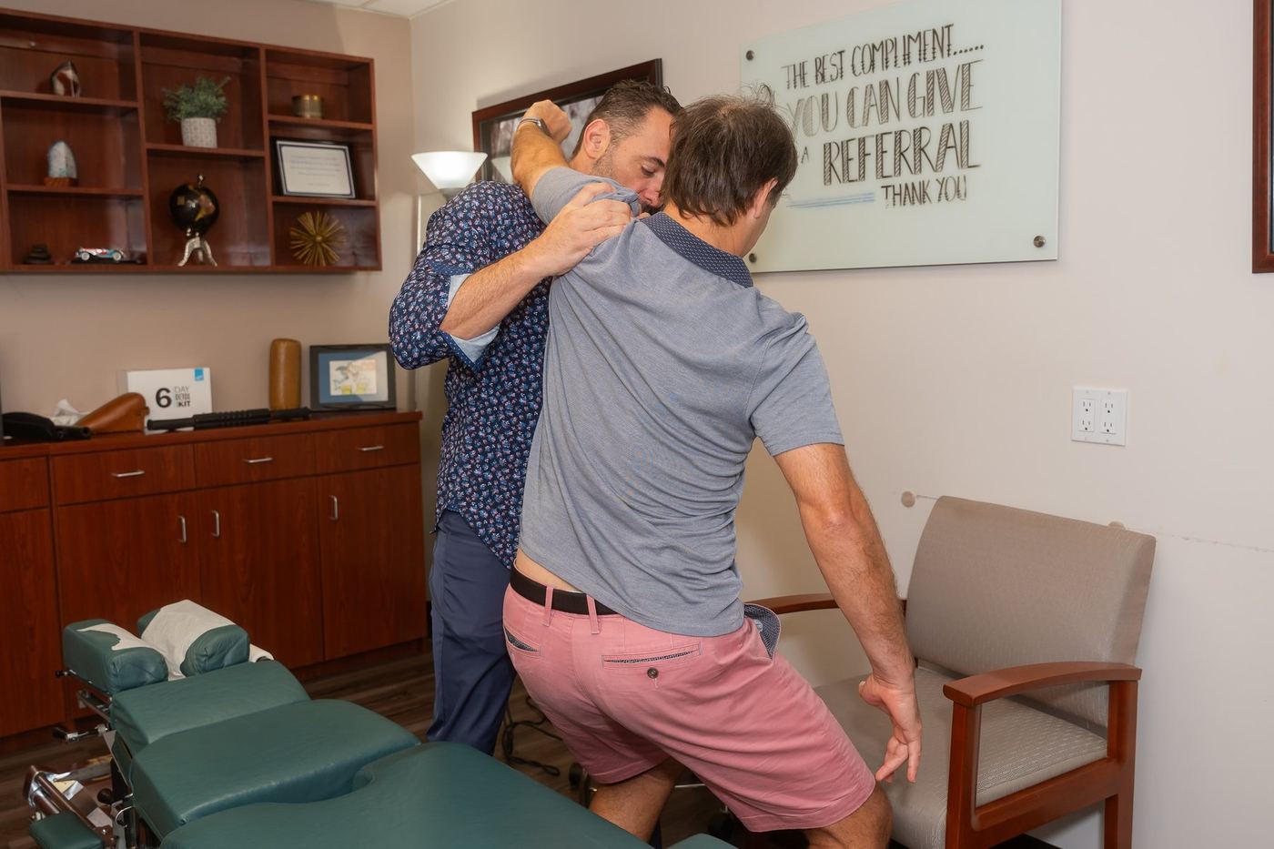 Dr. Edward Esposito performing a standing adjustment, arms wrapped around a patient's torso.